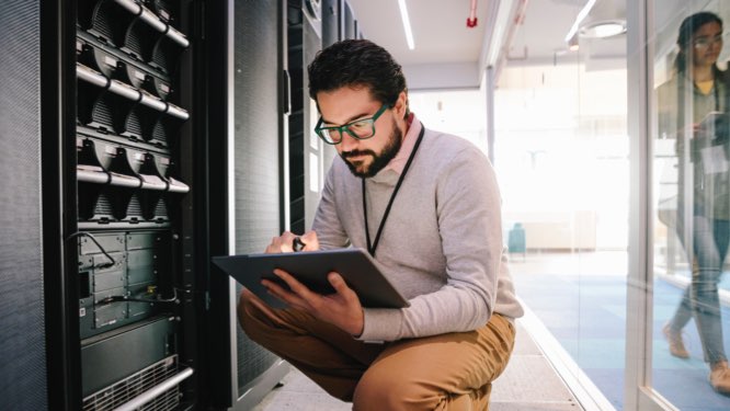 IT professional looking at a tablet while kneeling in front of server racks